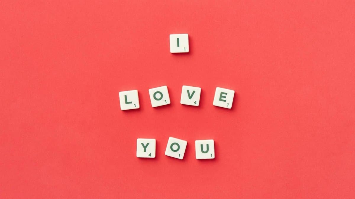 Scrabble tiles arranged to spell 'I Love You' on a vibrant red background, top view.