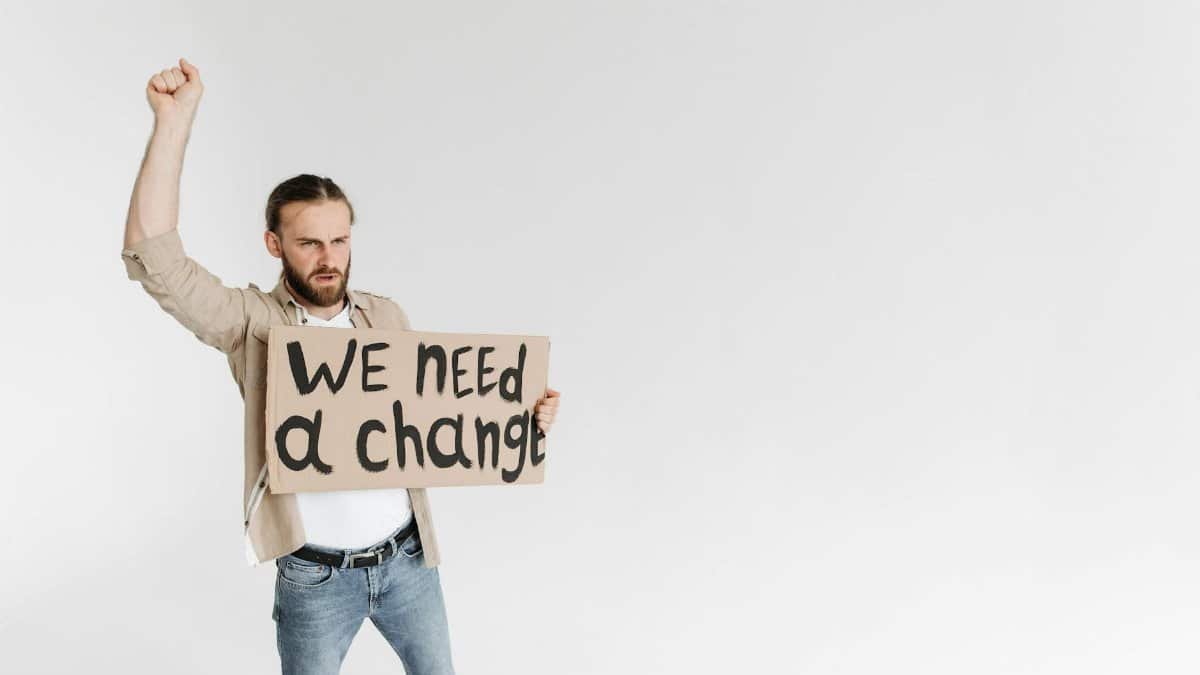 Man holding a 'We Need a Change' sign with raised fist, isolated background.