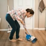 An Asian woman performing cleaning chores by sweeping the floor indoors.