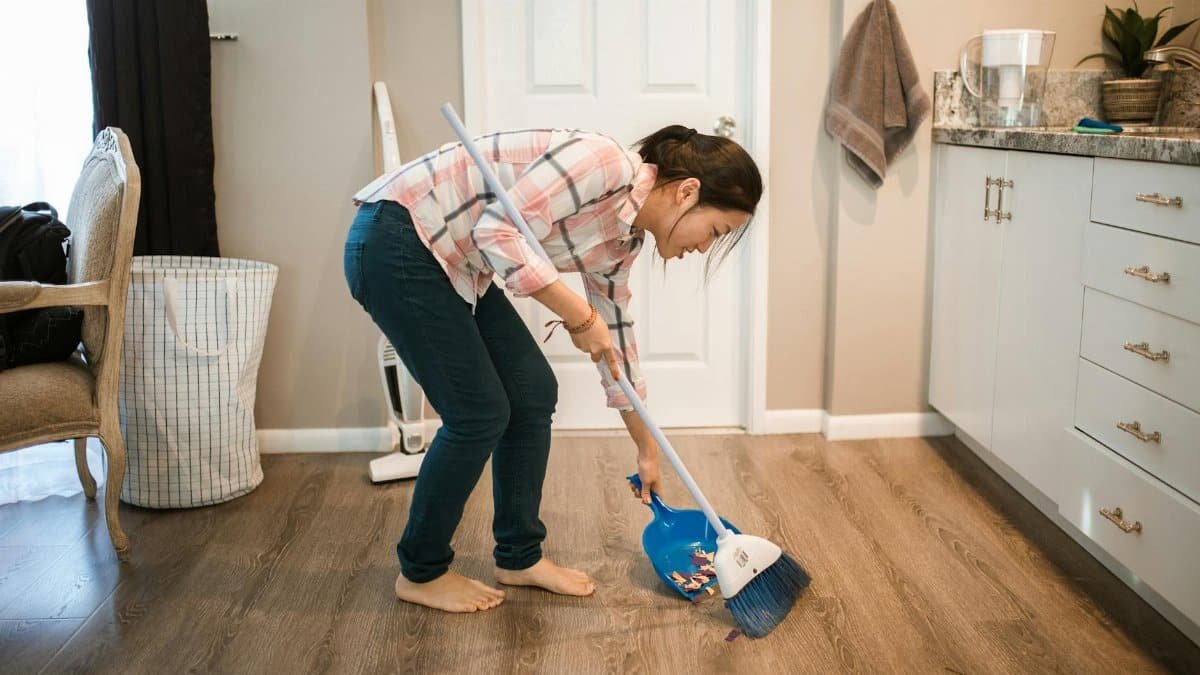 An Asian woman performing cleaning chores by sweeping the floor indoors.