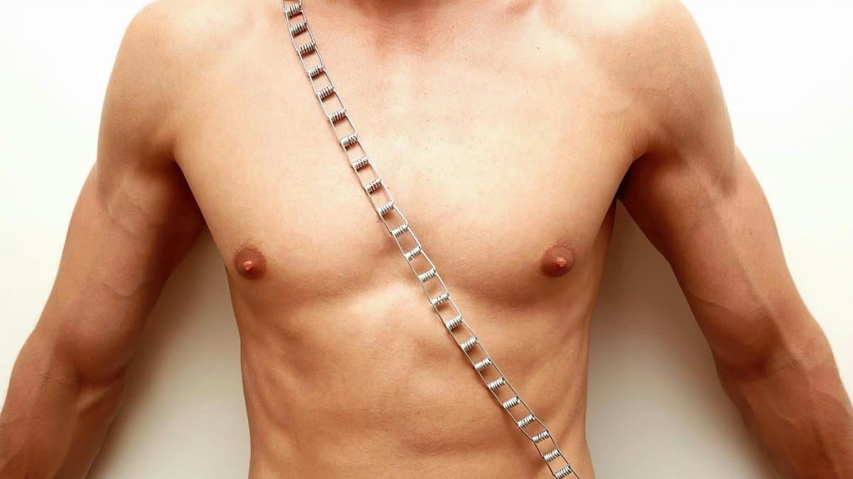 Close-up of a muscular male torso adorned with a stylish chain against a white background.