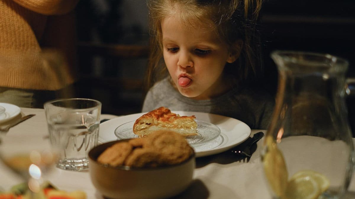 Young girl playfully sticking her tongue out at dinner, surrounded by food and family.