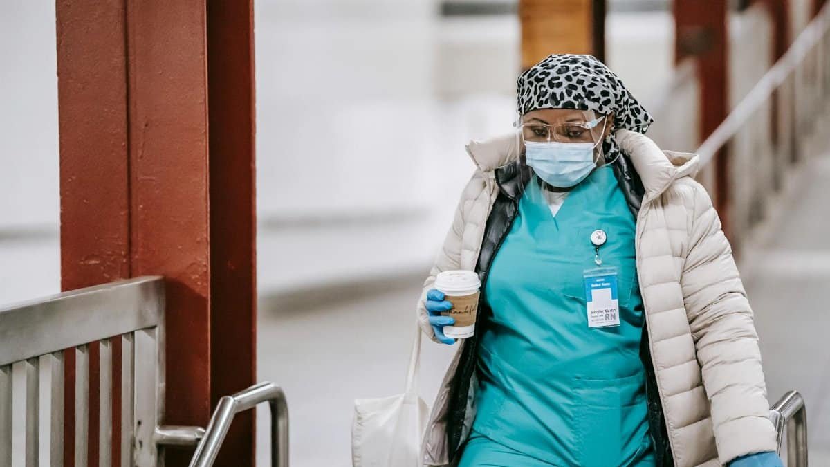 A healthcare worker in PPE and scrubs carrying a coffee cup, showcasing dedication during pandemic times.