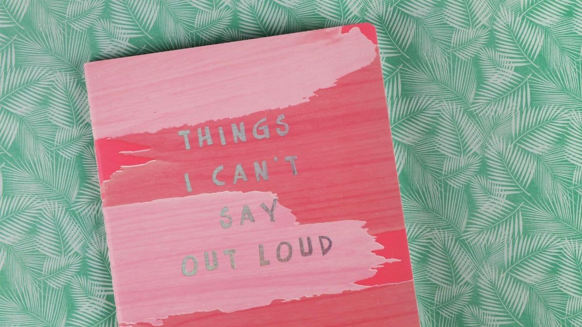 Pink notebook with the text 'Things I Can't Say Out Loud' on green leafy surface.