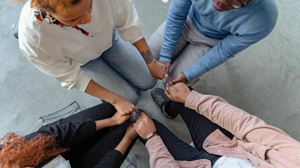 Four people sit in a circle holding hands, emphasizing unity and support in a therapy session.
