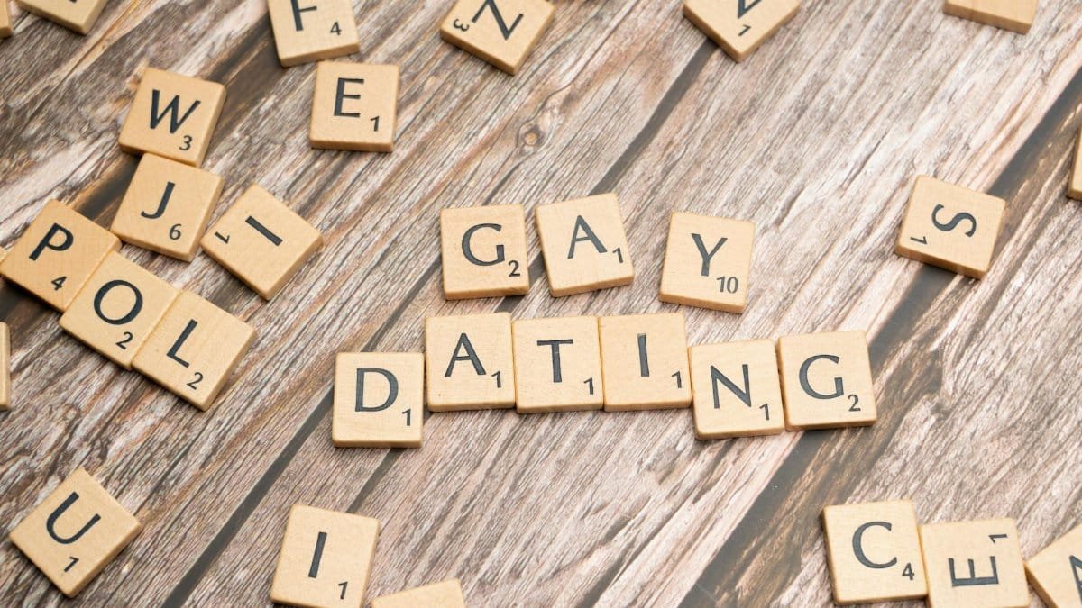 Scrabble tiles spelling 'Gay Dating' on a rustic wooden background, representing LGBTQ themes.