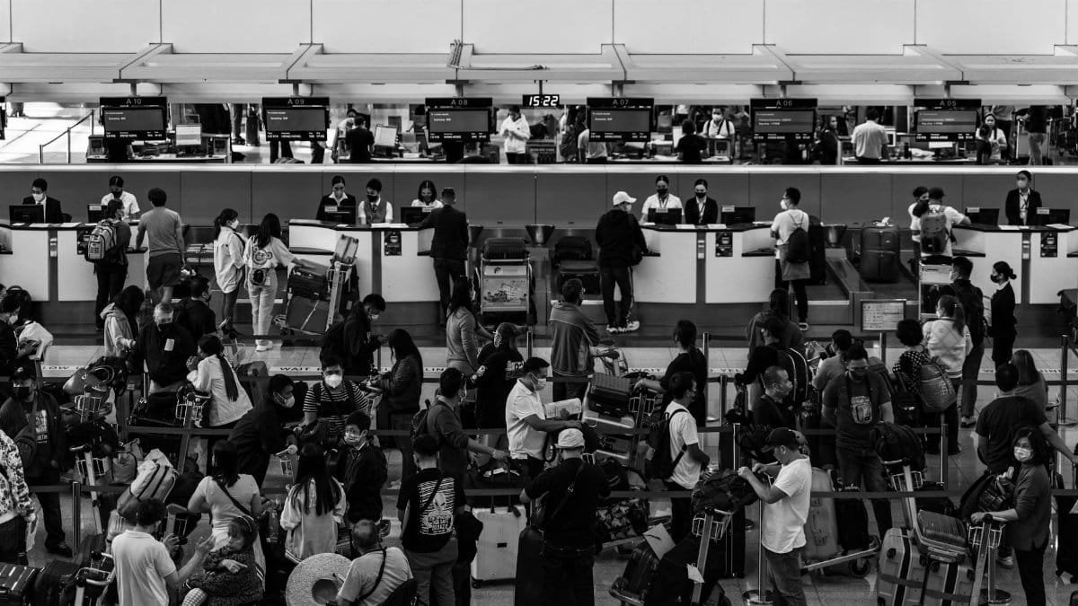 Black and white photo capturing a crowded airport check-in area filled with passengers and staff.