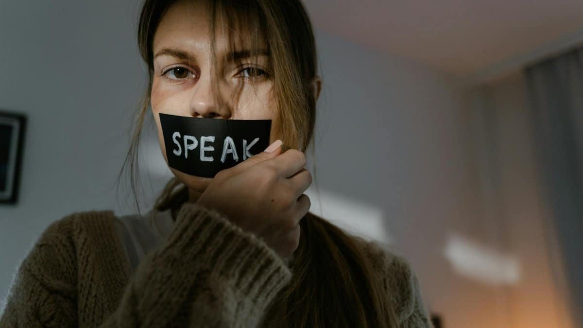 A woman with 'SPEAK' taped over her mouth, symbolizing silence and oppression.