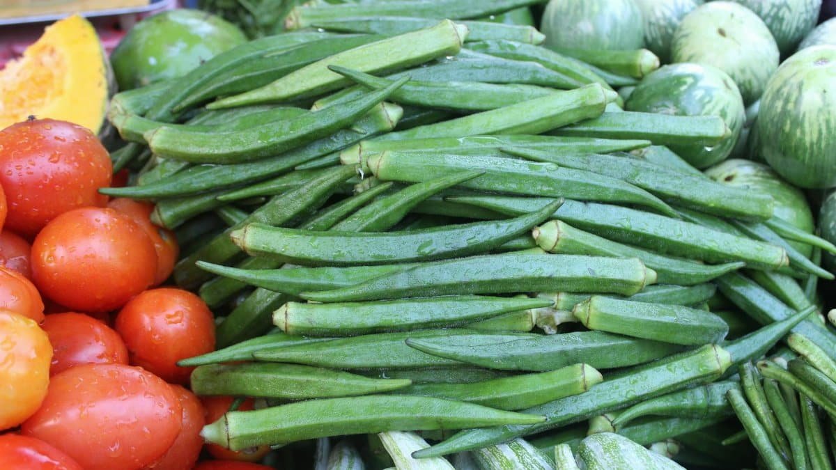 Colorful fresh vegetables including okra, tomatoes, and squash at a market stall.