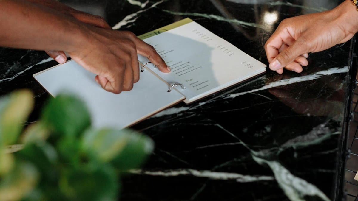 Hands pointing at menu on black marble counter inside a shop.