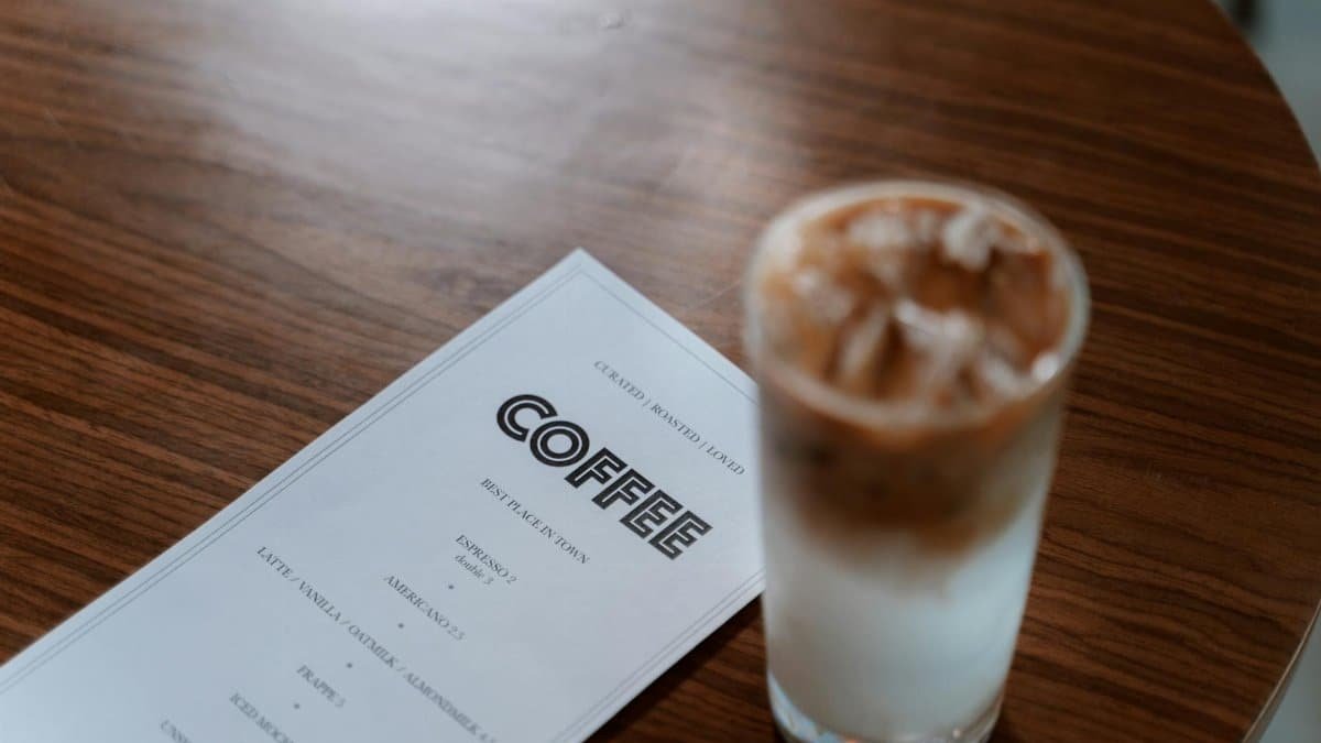A refreshing iced coffee next to a menu on a wooden table, perfect for cafe vibes.