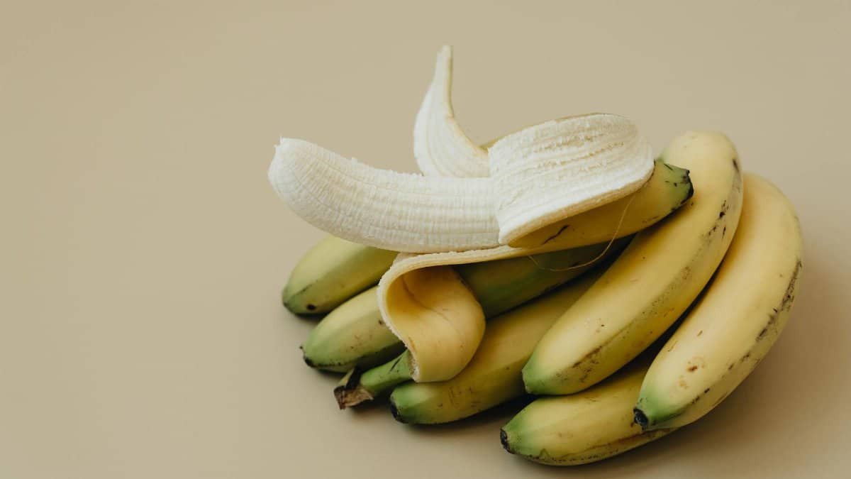 Close-up of a peeled banana on a cluster of fresh bananas, highlighting texture and freshness.