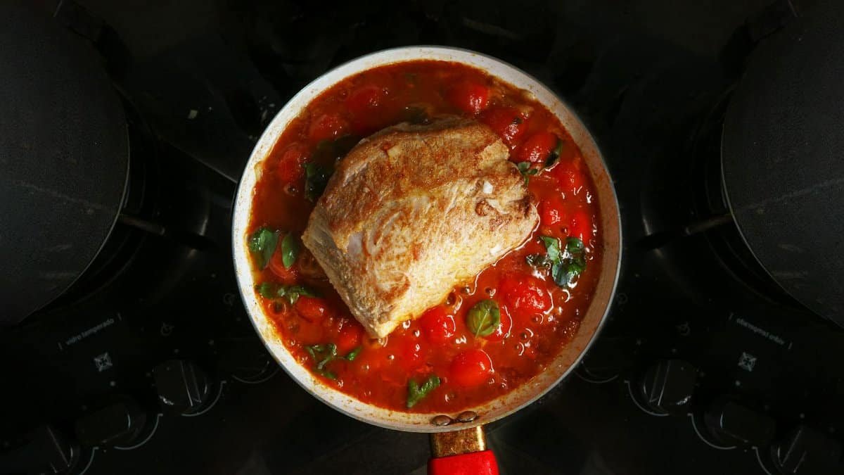 A savory roast beef cooked in rich tomato sauce with herbs, atop a stovetop.