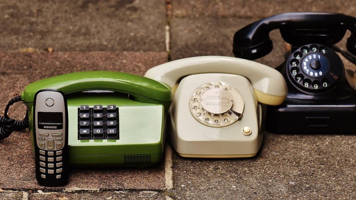 A variety of antique, vintage, and modern telephones displayed on pavement.