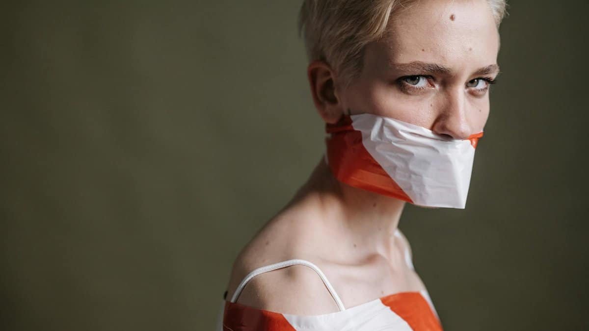 Artistic portrait of a woman with mouth covered by tape, symbolizing silence and oppression.