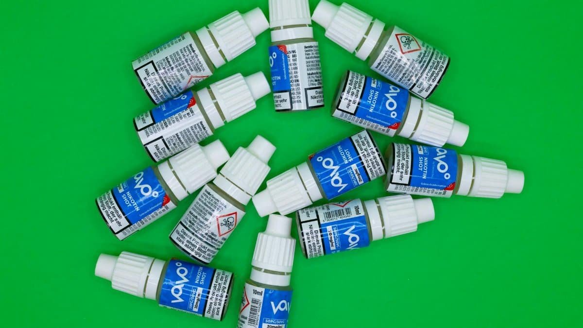 Top view of multiple nicotine vape shot bottles arranged on a green background.