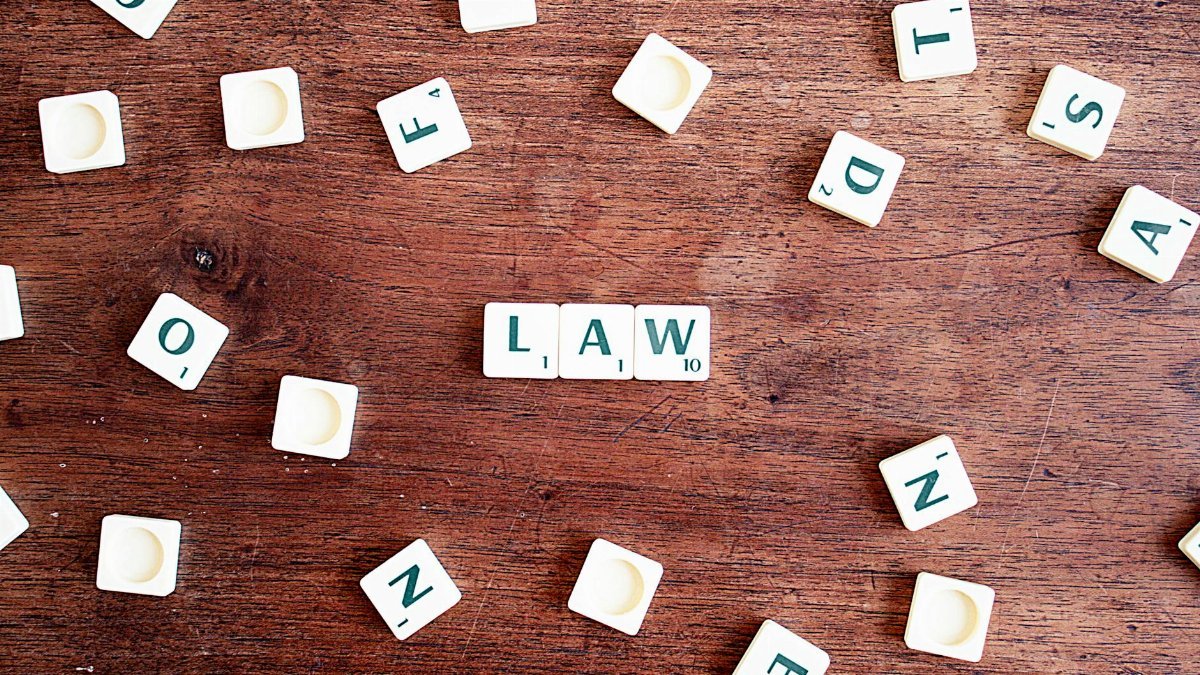 Scrabble tiles spelling 'LAW' on a wooden table, symbolizing connections to education and legality.