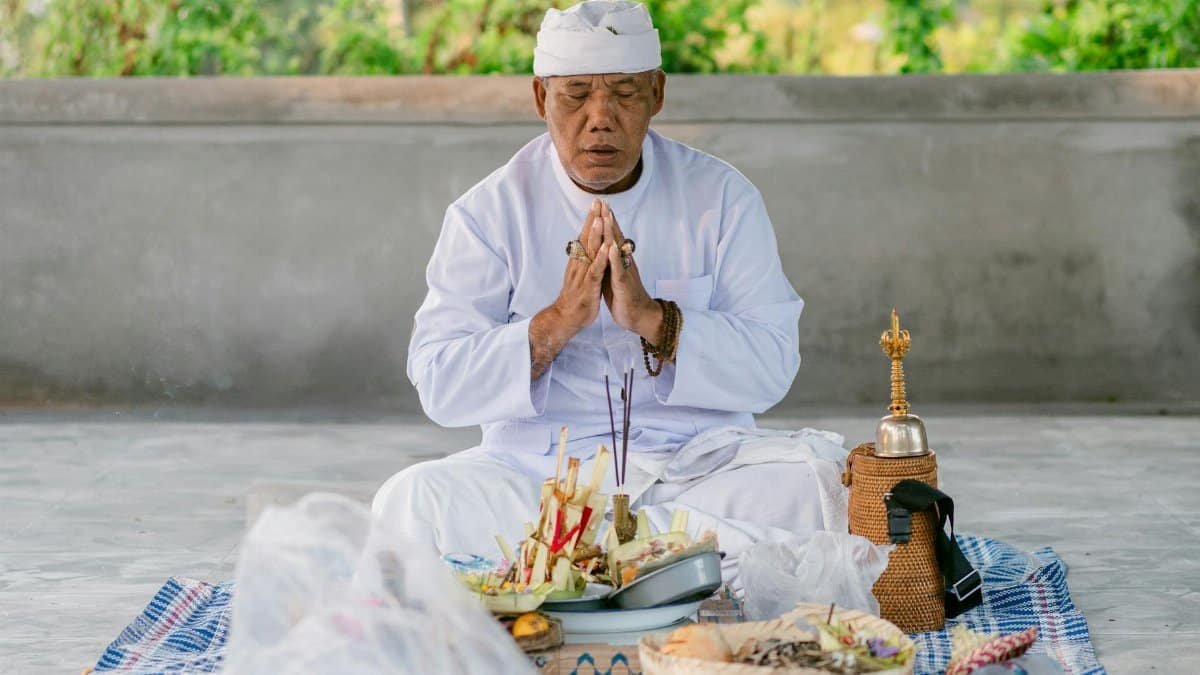 Senior priest in traditional attire performing a prayer ritual outdoors with offerings.