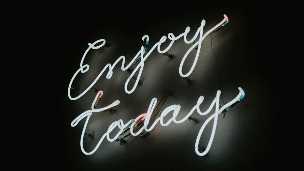 Neon sign with motivational message 'Enjoy Today' on a dark background.