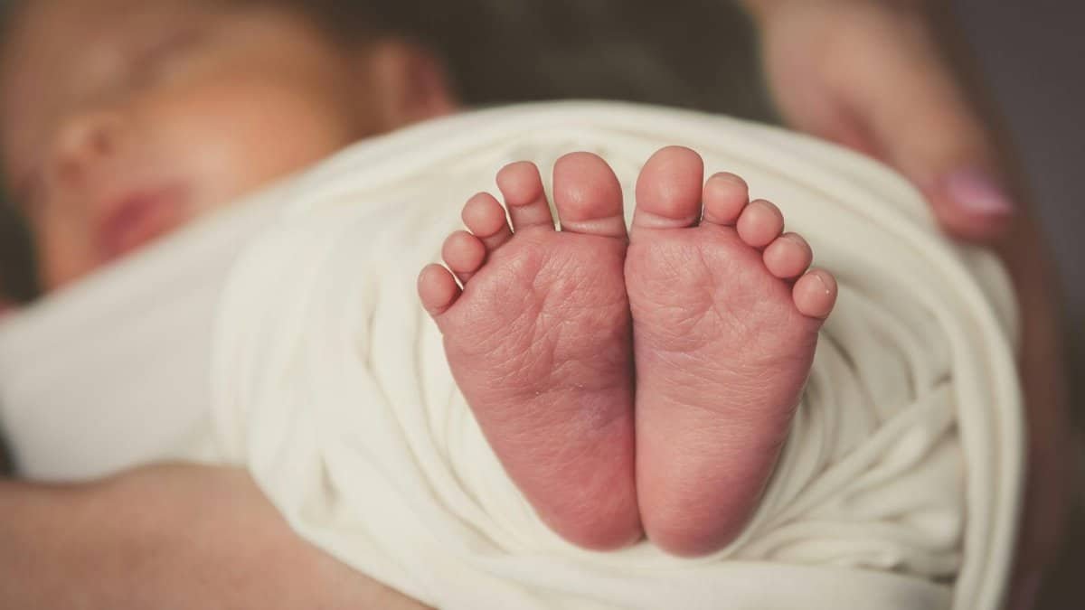 Adorable newborn baby feet wrapped in soft white blanket, capturing innocence and delicacy.