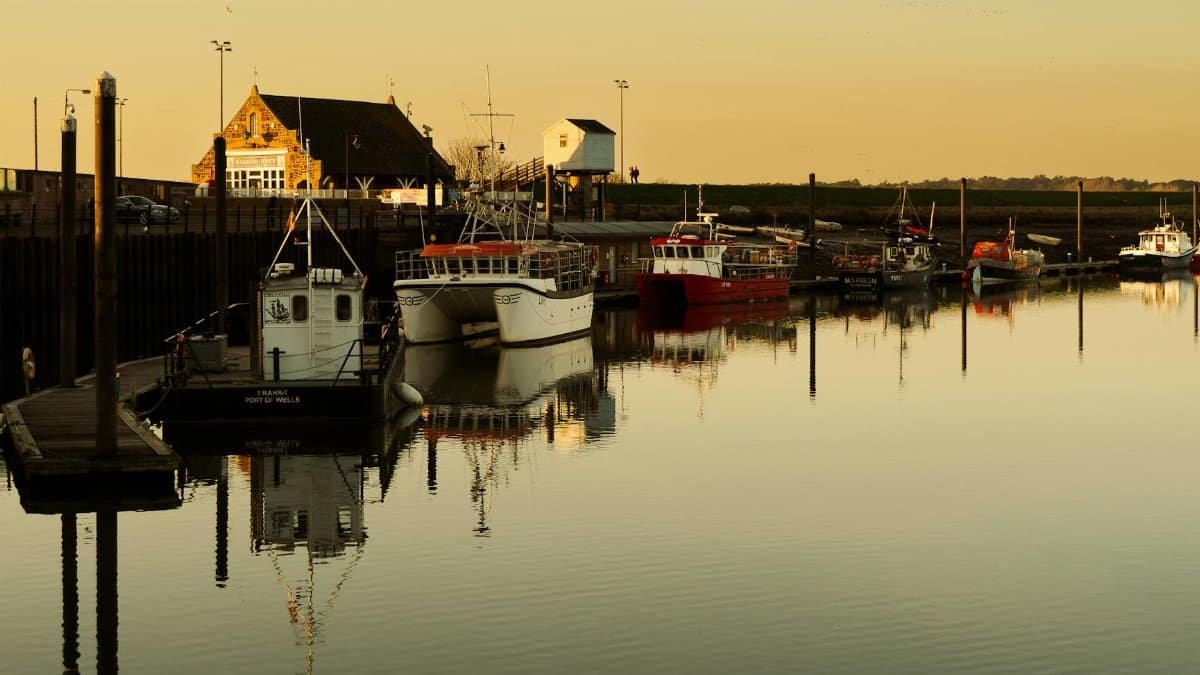 Calm waters and fishing boats at sunset in Wells-next-the-Sea harbor, England.