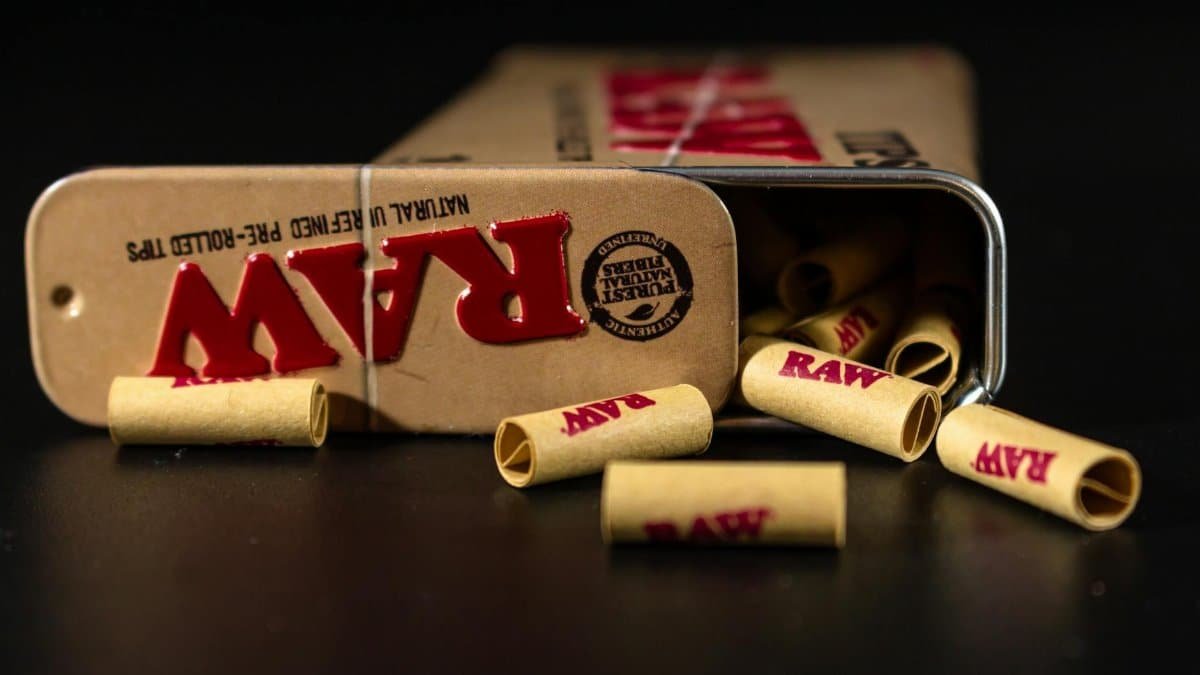 RAW pre-rolled tips spilling from a metal tin on a dark surface, close-up view.
