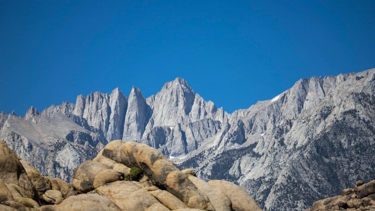 Capture the majestic Mount Whitney with its rugged peaks against a clear blue sky, showcasing natural beauty.