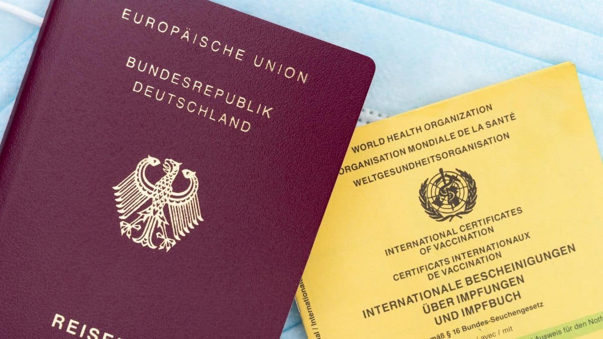 Close-up of a German passport, vaccination card, and face mask, symbolizing travel and health documentation.