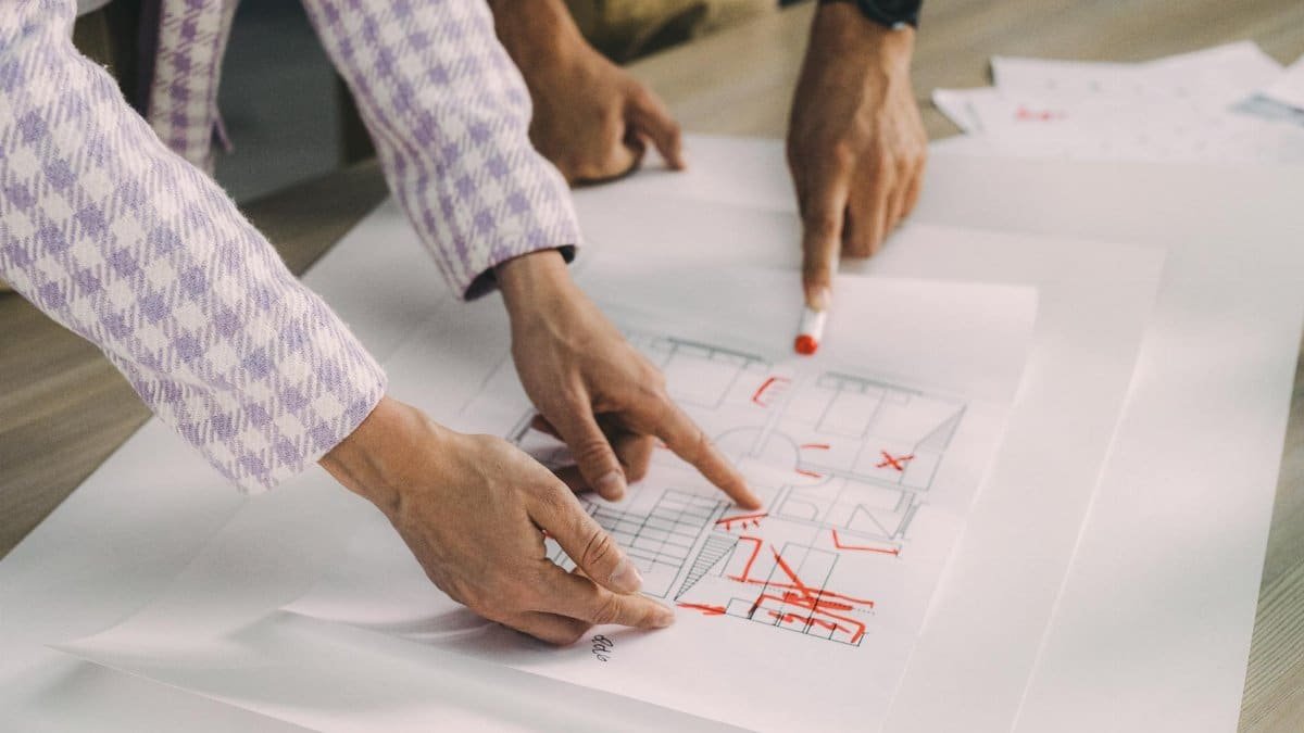 Two people discussing an architectural floor plan with red markings on paper.