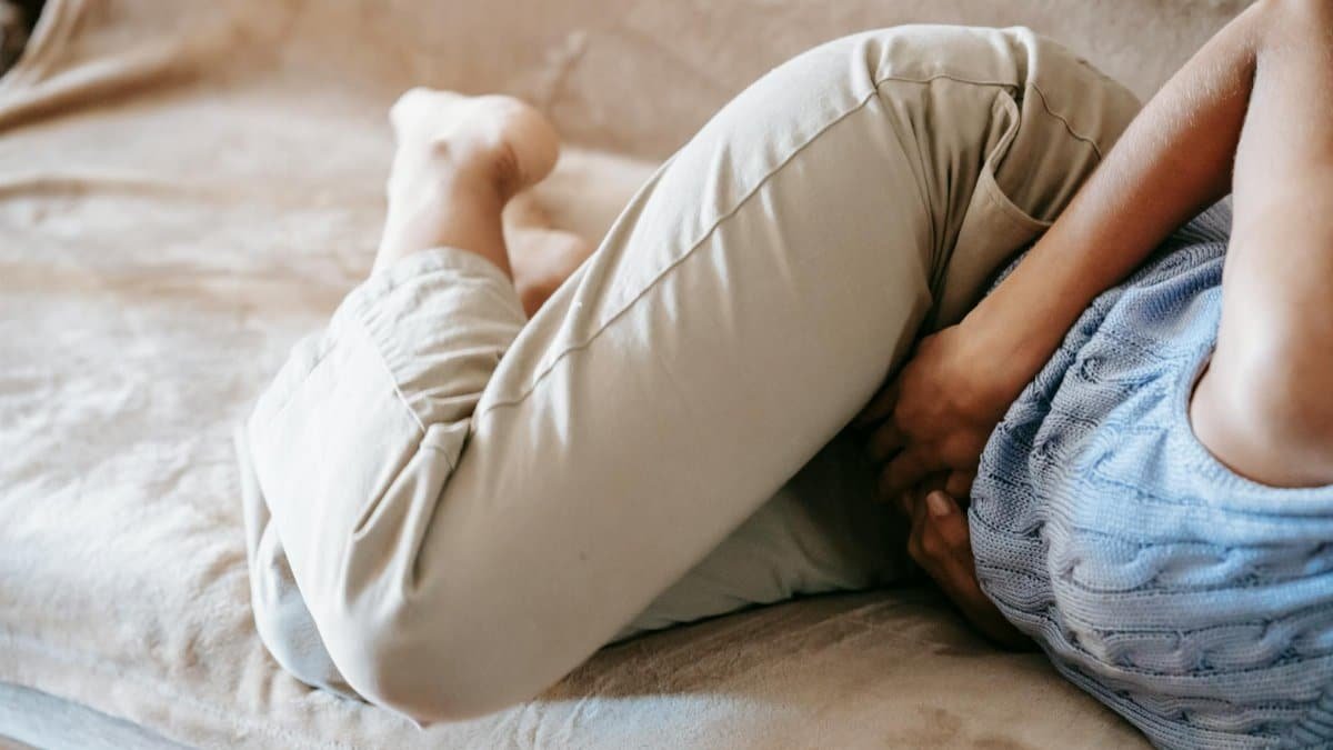 A person in pain holding their stomach while lying on a couch indoors, suggesting discomfort or illness.