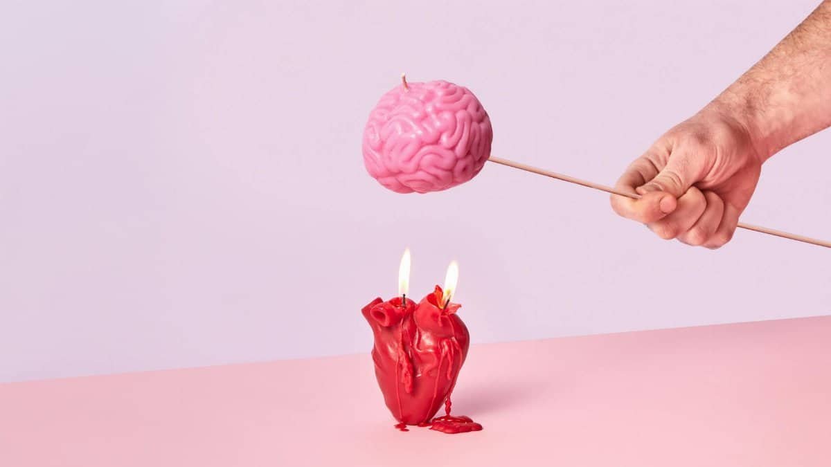 Artistic photo of a hand holding a brain-shaped candle while a heart candle burns below, symbolizing intellect vs emotion.