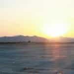 Tranquil view of an airport runway with the sun rising over distant mountains, casting a gentle glow.