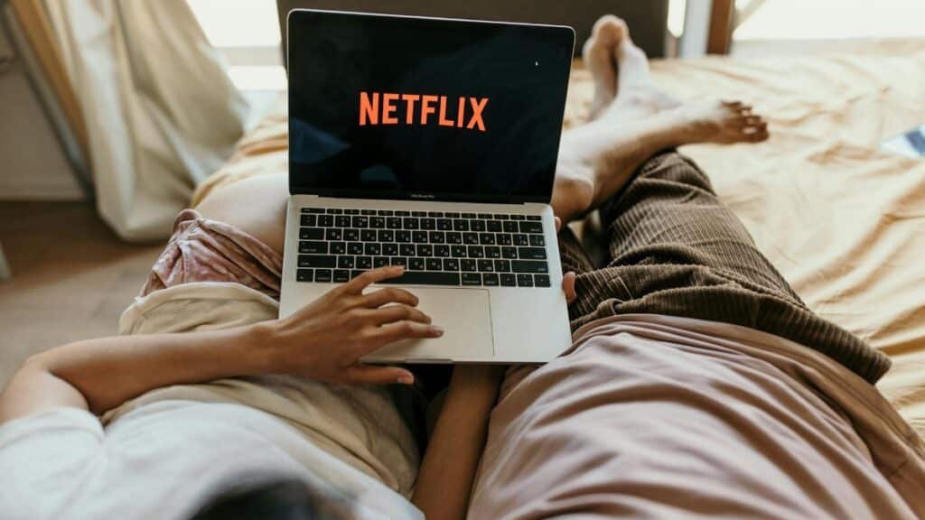 A couple lying comfortably in bed watching Netflix on a laptop, enjoying leisure time together indoors.