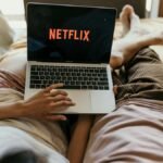 A couple lying comfortably in bed watching Netflix on a laptop, enjoying leisure time together indoors.