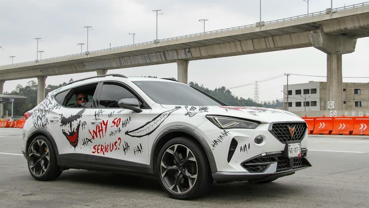 White SUV decorated with Joker-inspired art on a highway under bridge.