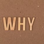 Wooden letters spelling 'WHY' on a brown cardboard background. Ideal for concepts of questioning and curiosity.