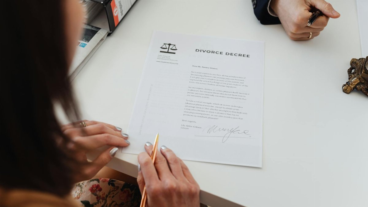 A close-up shot of two people signing a divorce decree at a law office table.