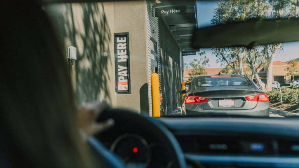 A driver's perspective waiting at a fast food drive-thru queue in daylight.