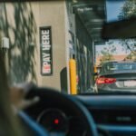 A driver's perspective waiting at a fast food drive-thru queue in daylight.