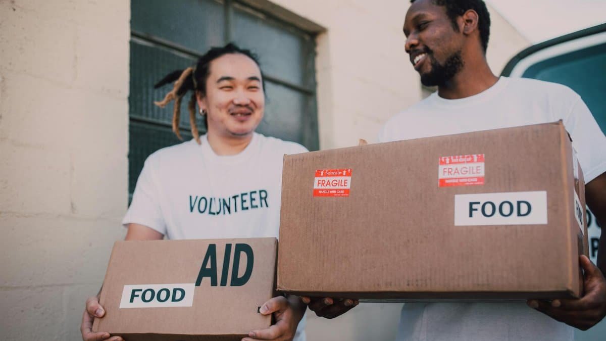 Two volunteers carrying aid boxes labeled food, showing community support and charity efforts.