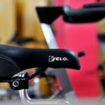 Detailed focus on a black bicycle saddle with gym equipment in the background.