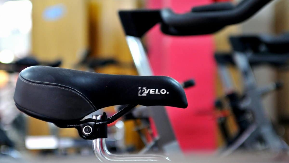 Detailed focus on a black bicycle saddle with gym equipment in the background.