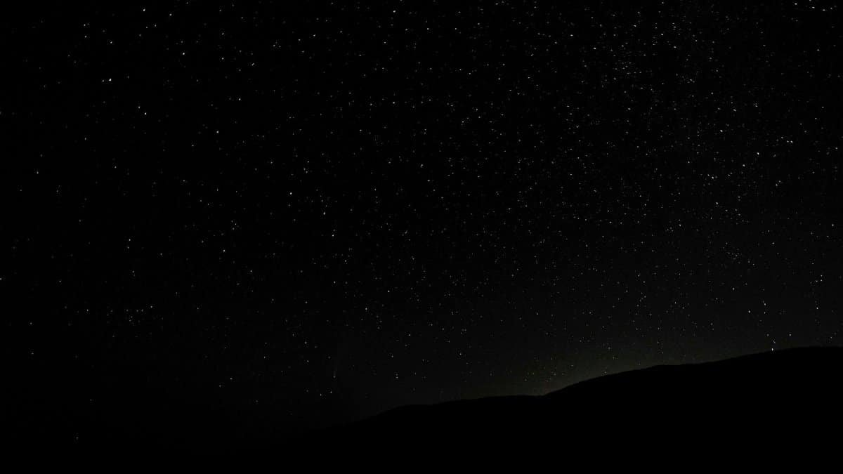Dark endless sky covered with shining luminous stars above silhouette of hill at night
