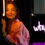 Smiling teenager in a studio with neon lights and ice cream sign, vibrant youth culture.