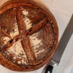 Close-up of a freshly baked artisan sourdough bread loaf with a rustic crust on a cloth with knife.