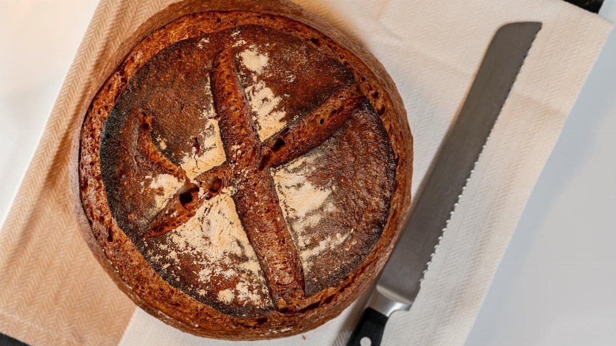 Close-up of a freshly baked artisan sourdough bread loaf with a rustic crust on a cloth with knife.