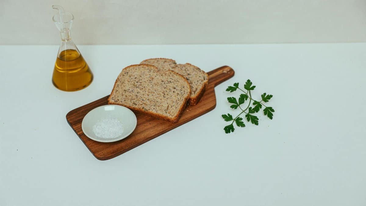 A minimalist still life of wheat bread, olive oil, and parsley on a wooden board.
