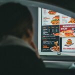 A woman in a car views the menu at a fast food drive-thru, ready to order her meal.