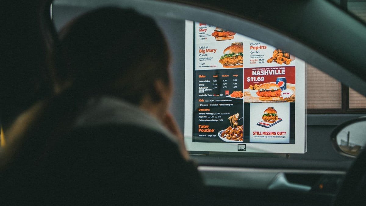 A woman in a car views the menu at a fast food drive-thru, ready to order her meal.