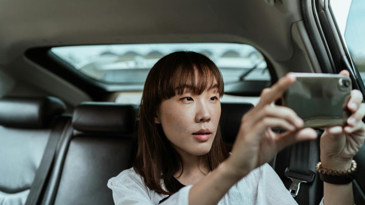 A woman taking a photo with her smartphone from the backseat of a car.